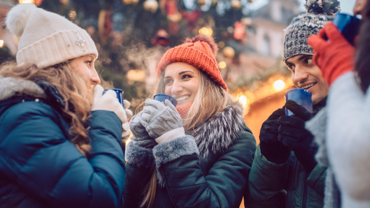 Group of friends drinking mulled wine in the cold on a Christmas Market with fun and laughter