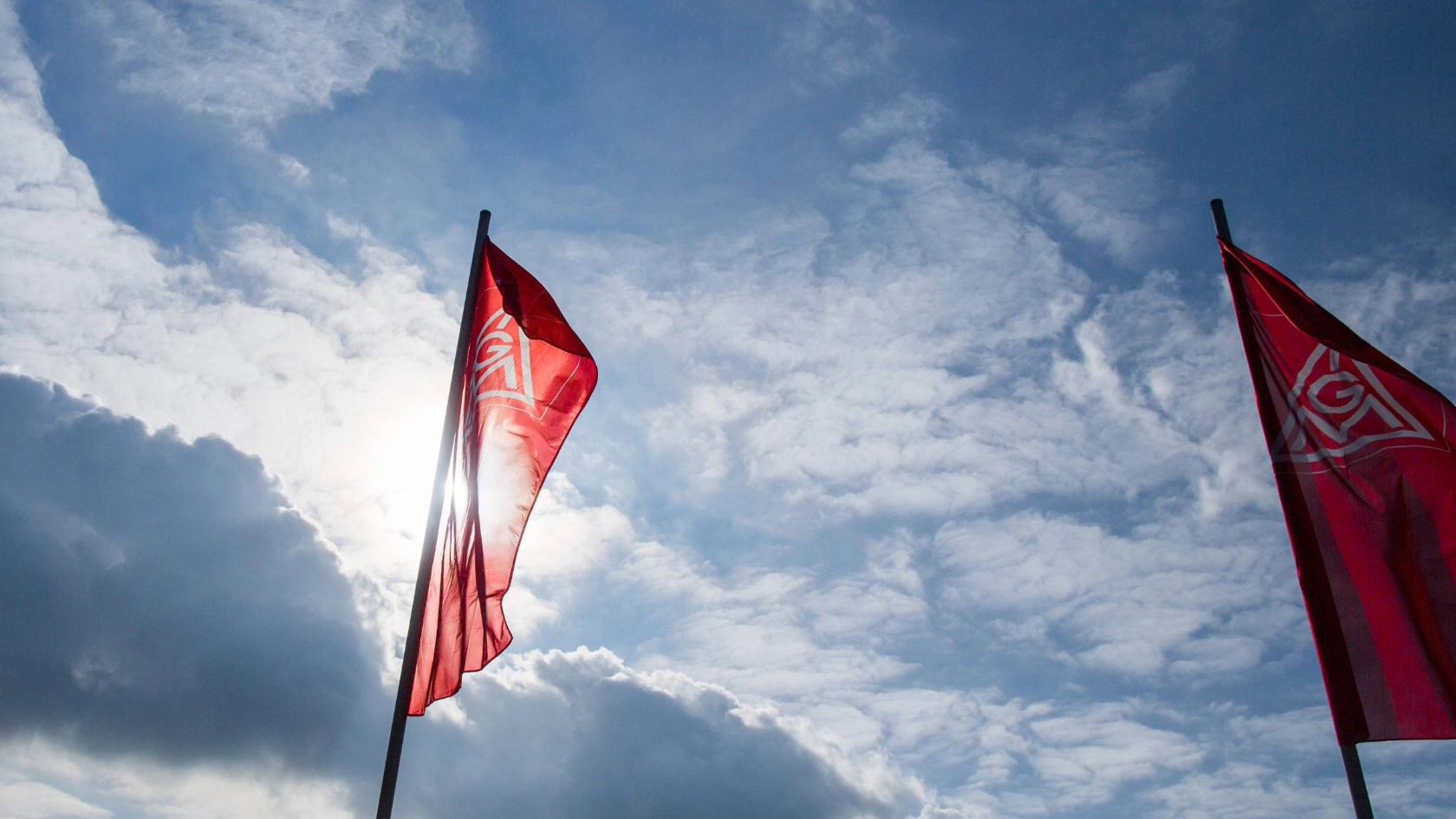 IG Metall-Fahnen vor leicht bewölktem Himmel.